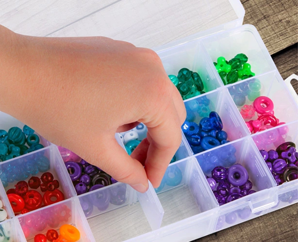 Child's hand reaching into storage box containing beading jewels.